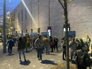 Verschillende mensen lopen 's avonds op straat rondom grote fotokubussen.