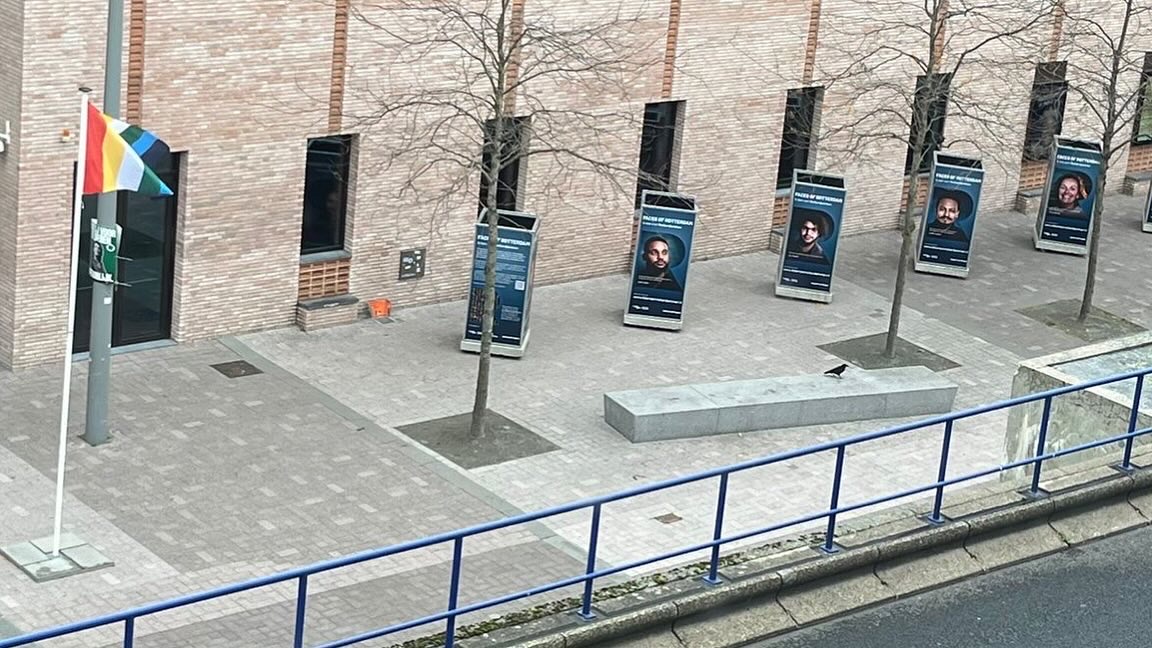 Je ziet een vlag links en daarnaast vijf fotokubussen met grote portretten daarop